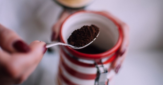A person picking up coffee grounds with a spoon